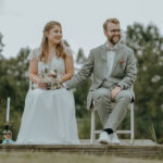 Ein Hochzeitspaar sitzt auf eine Stuhl-. Die Braut hat einen Strauß Blumen in der Hand