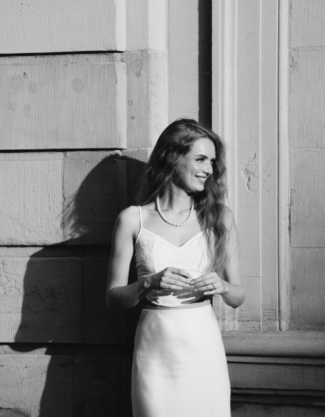 Frau steht vor einer Hauswand. In schwarz-weiß. Sie lacht zur Seite und die Sonne strahlt sie an. Sie wirft ein Schatten.